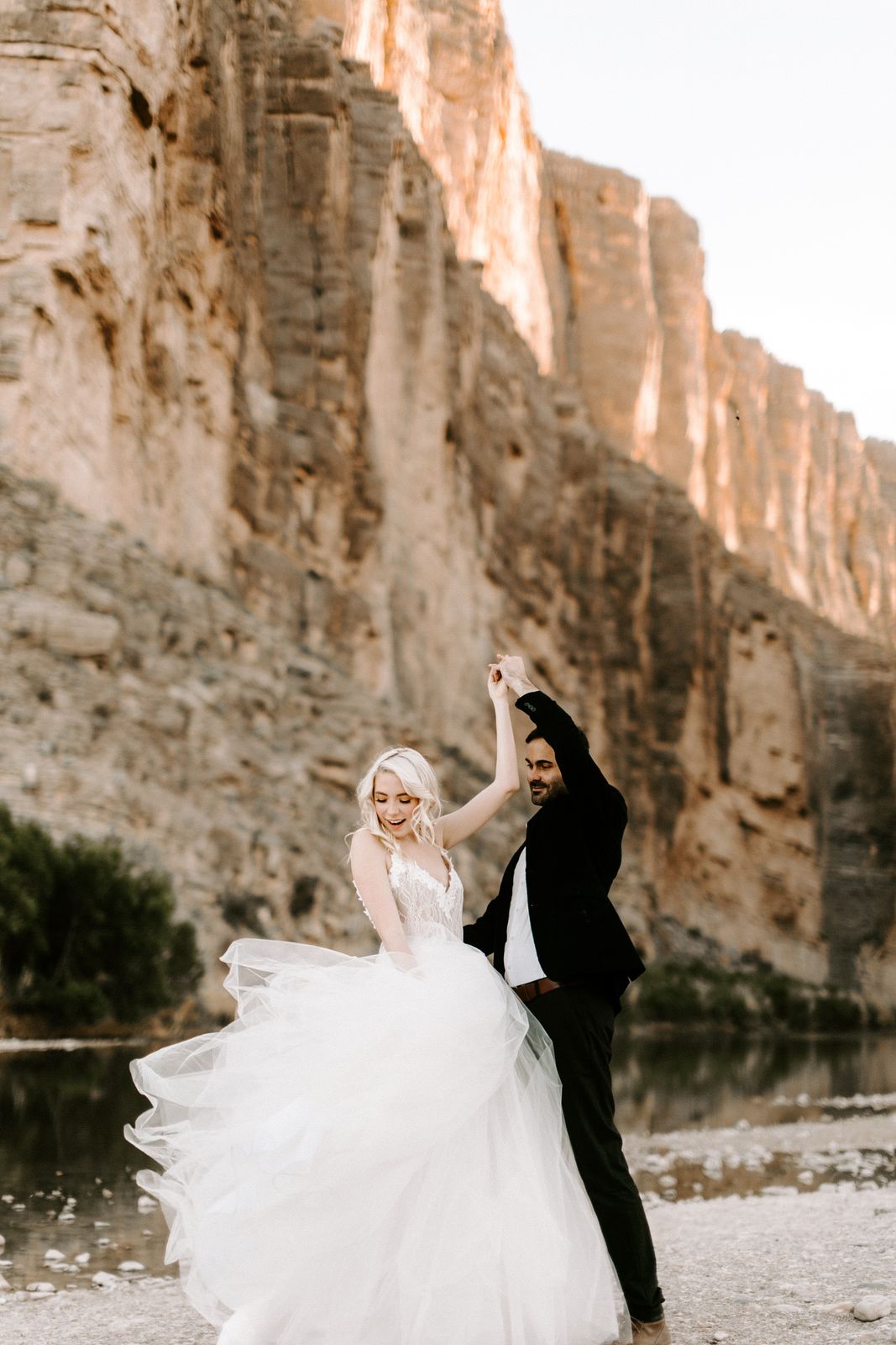 A bride twirling beside her groom below the canyon walls of Big Bend