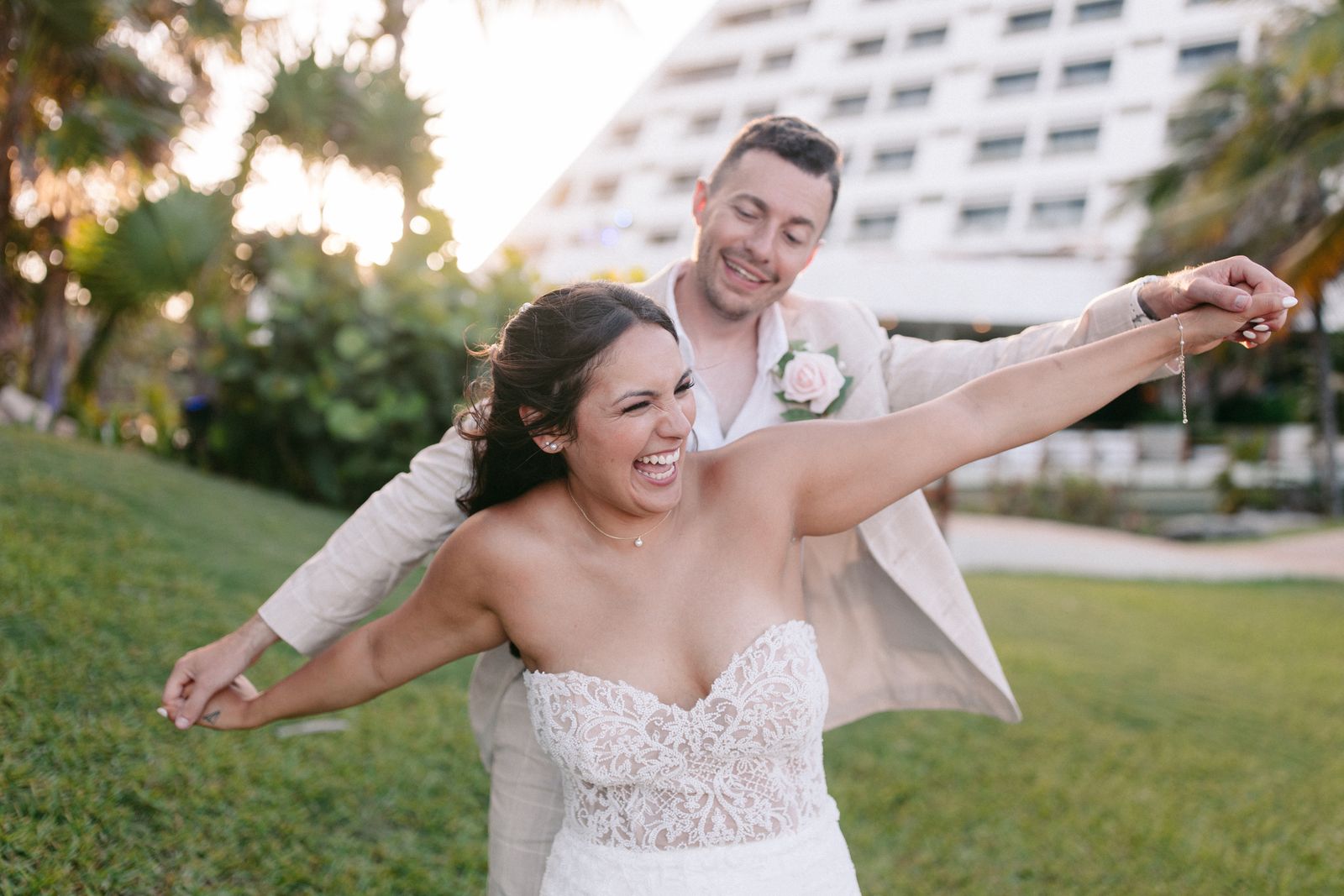 A laughing bride throwing her arms wide in front of her groom at a beach resort