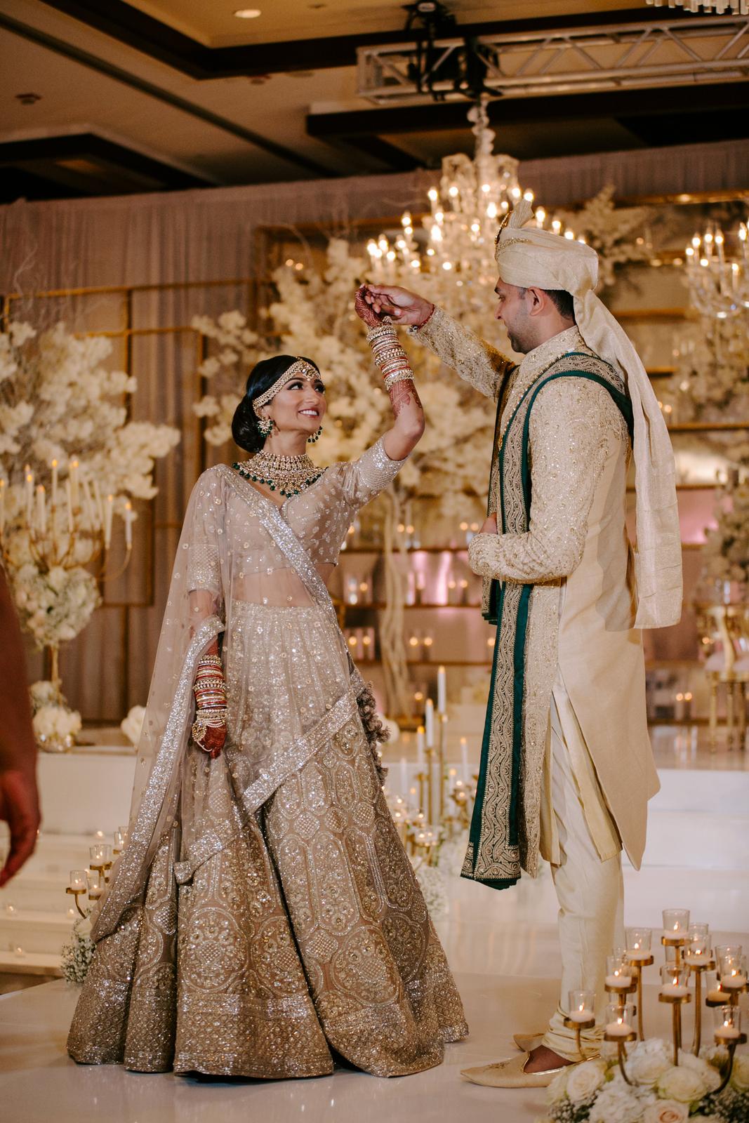 A bride and groom in gold and ivory dancing under a chandelier