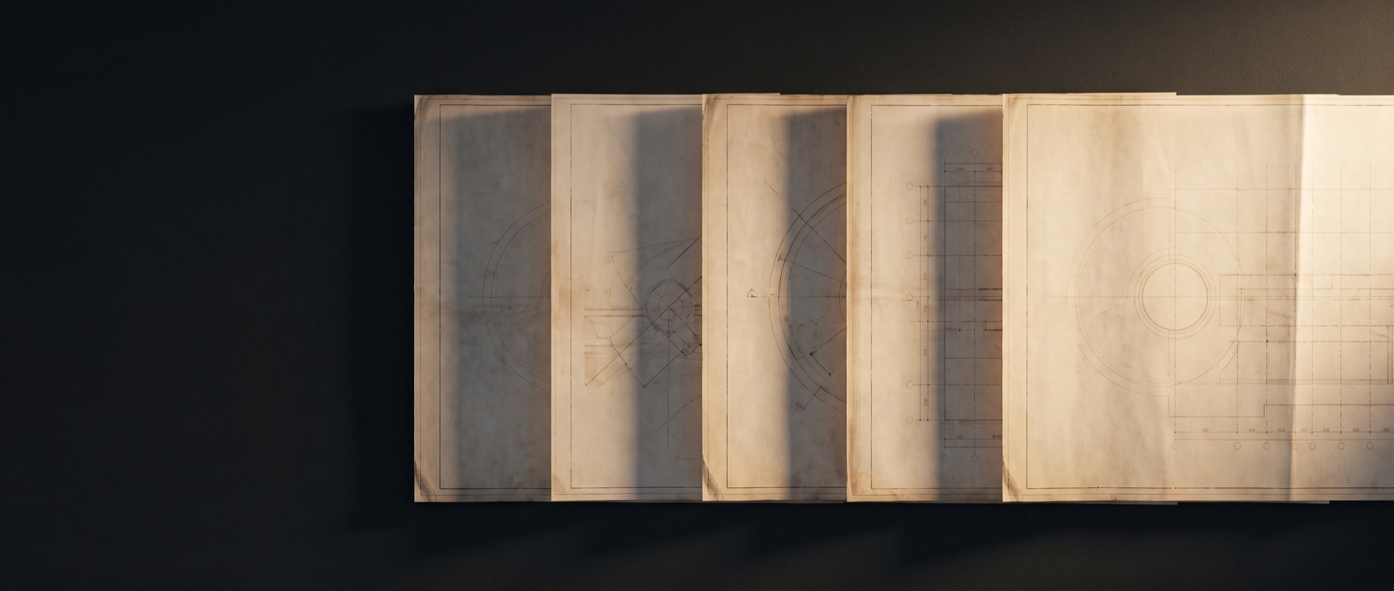 Four architectural drawing sheets laid in a precise row on a dark surface, seen from above.