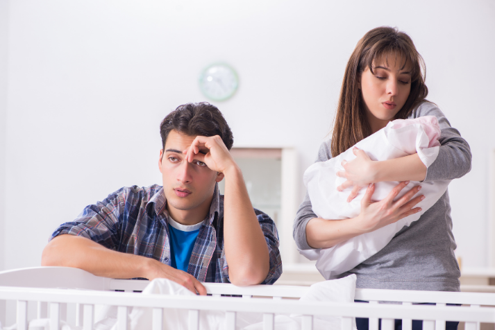 A mother soothes a baby while the father looks distressed