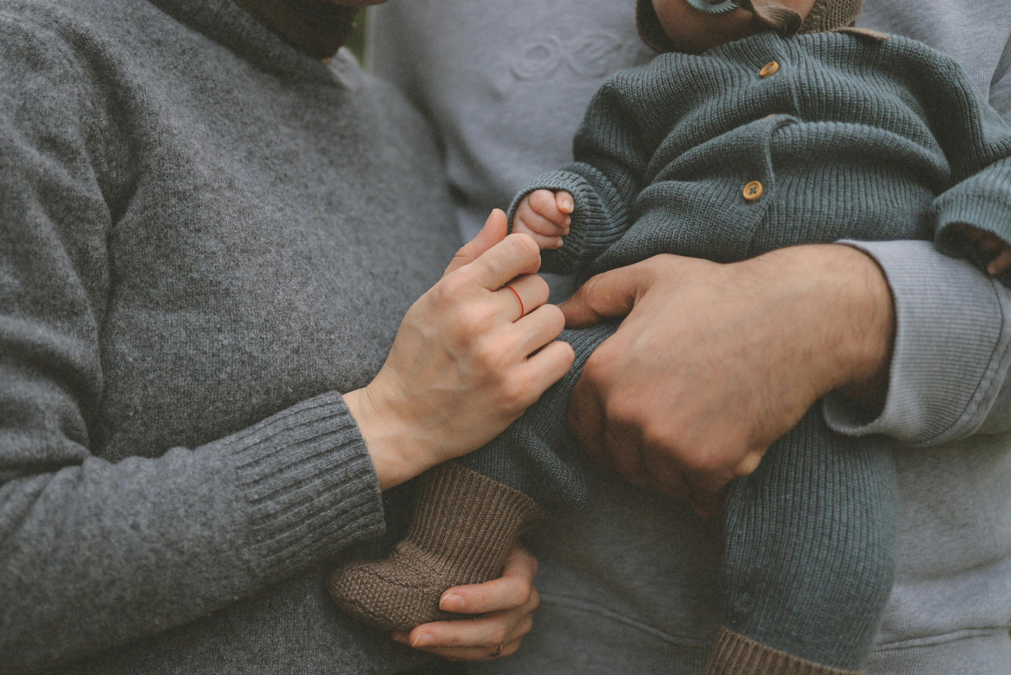 A man and woman gently hold a baby dressed in a cozy sweater, smiling at each other in a warm, loving moment.
