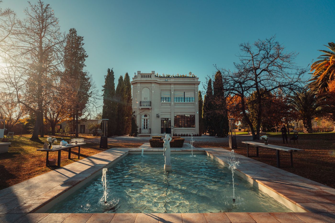 The Luigi Bosca winery in Mendoza at golden hour, tables set for a tasting beside the reflecting pool