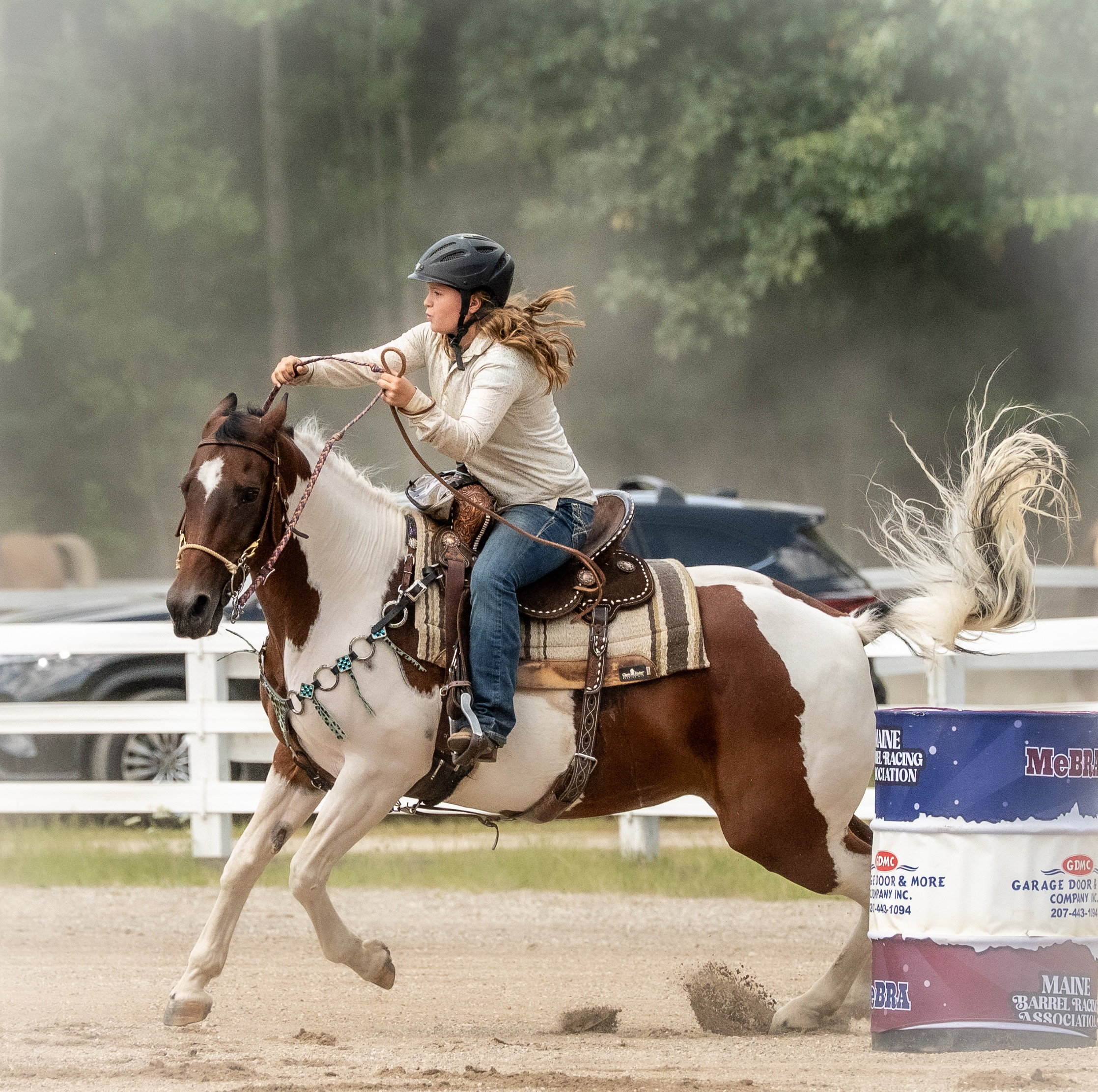 A woman in elegant riding attire standing beside a dark horse in a sunlit Connecticut arena during a horse and rider photography session
