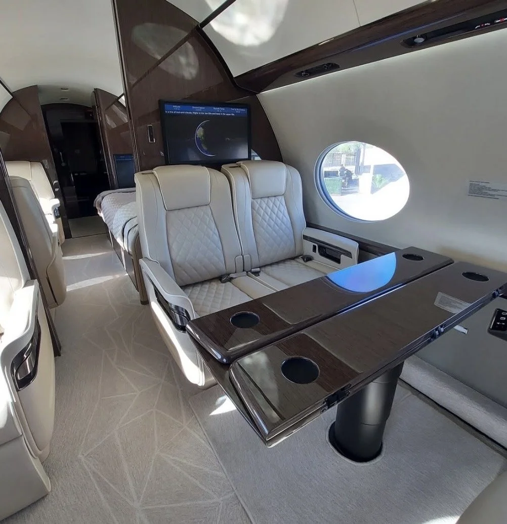 Detailed private aircraft cabin interior with cream leather seats and wood tray tables