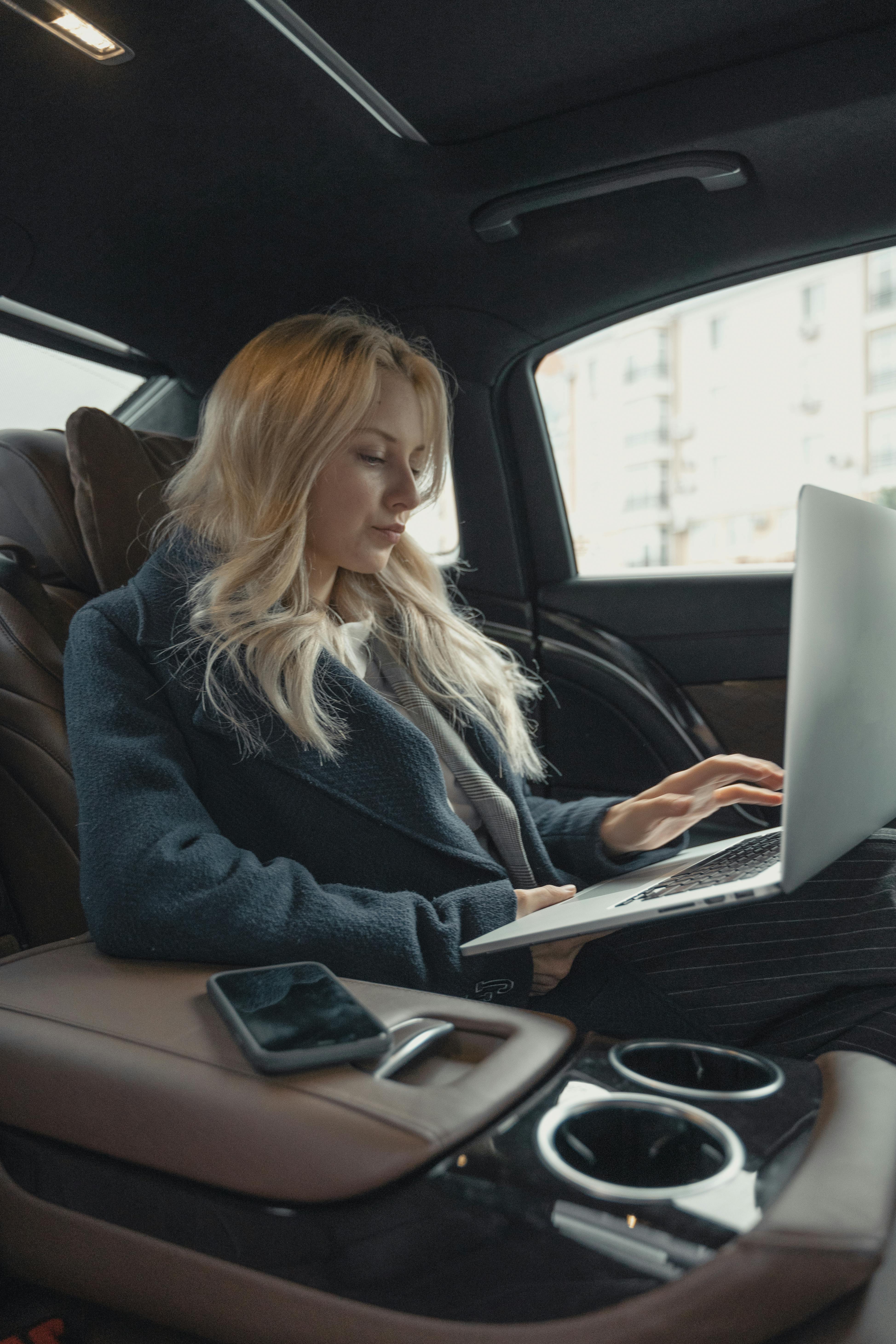 A picture of a woman holding a laptop while sitting in a car.