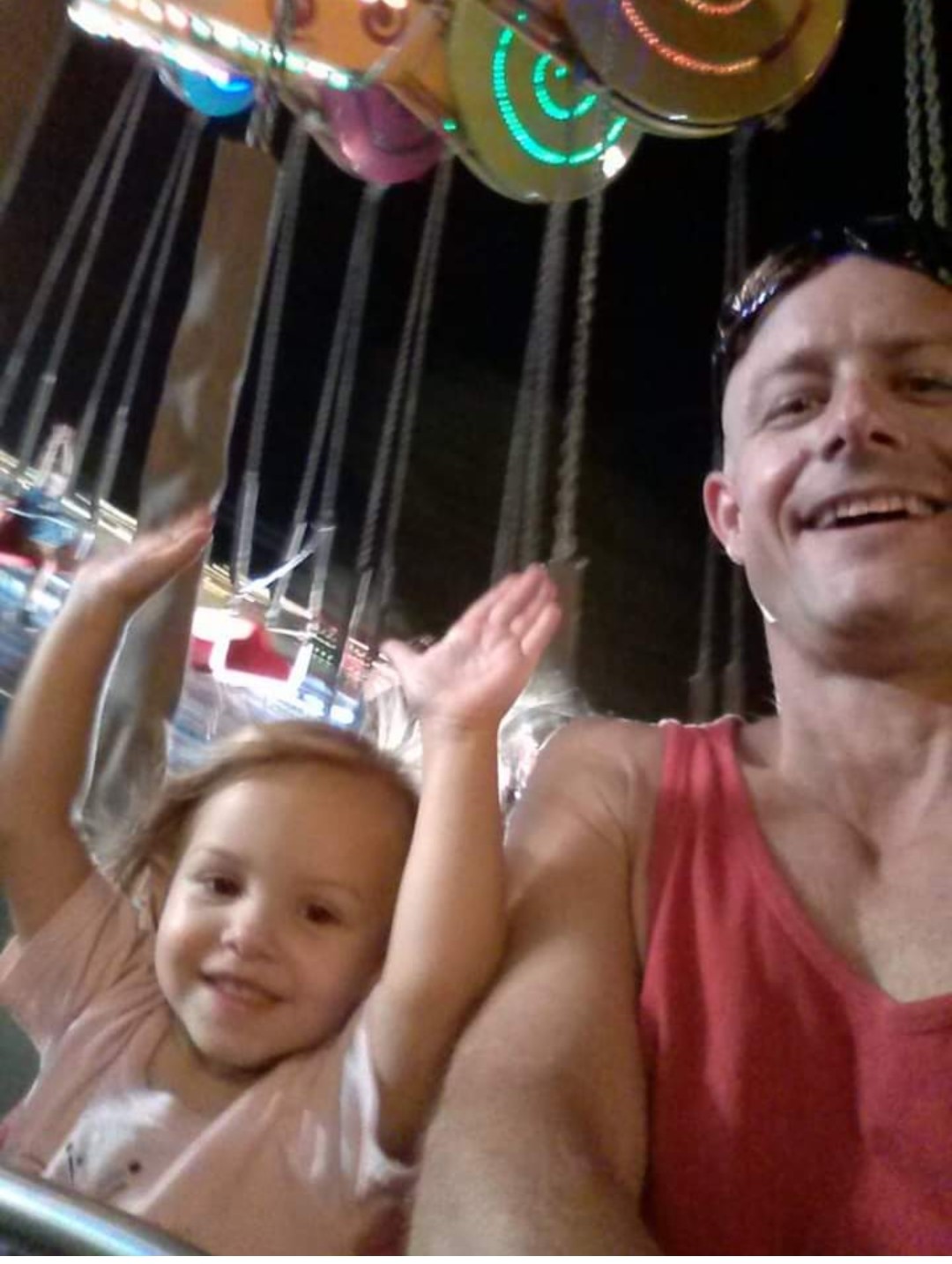 George and Taylor on a carnival ride at night — hands up, both laughing with pure joy