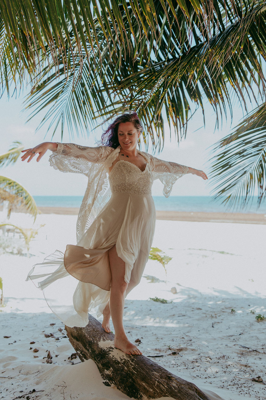 Annie on a beach in a flowing cream dress, arms open wide under the palms