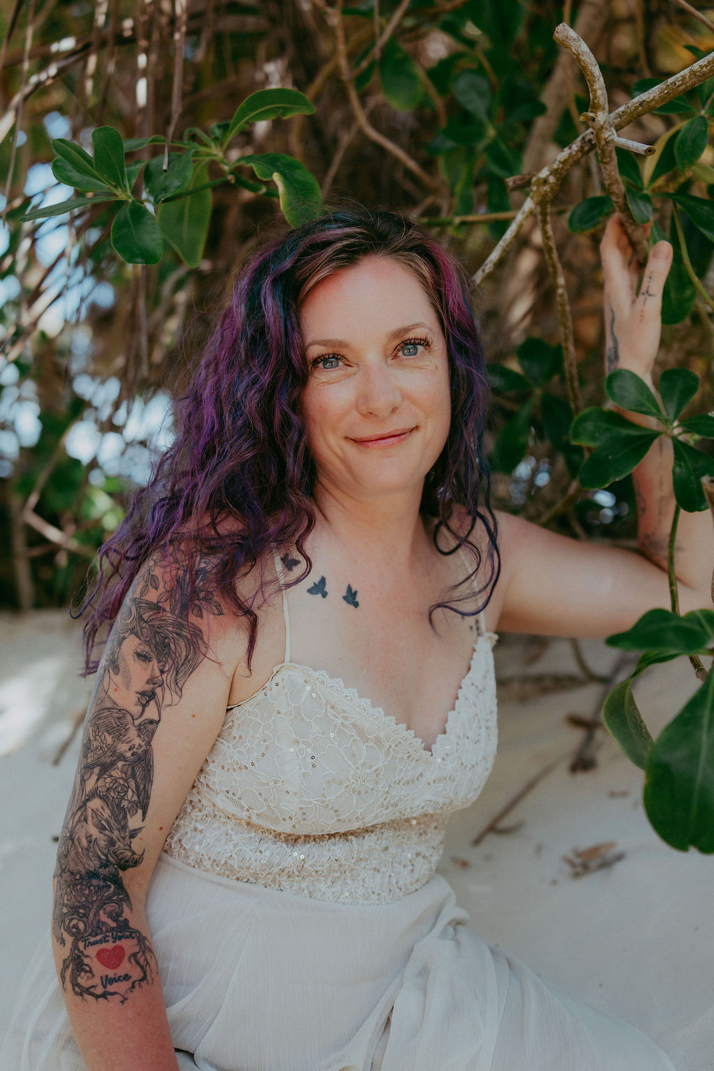 Annie smiling, seated in the sand among green leaves