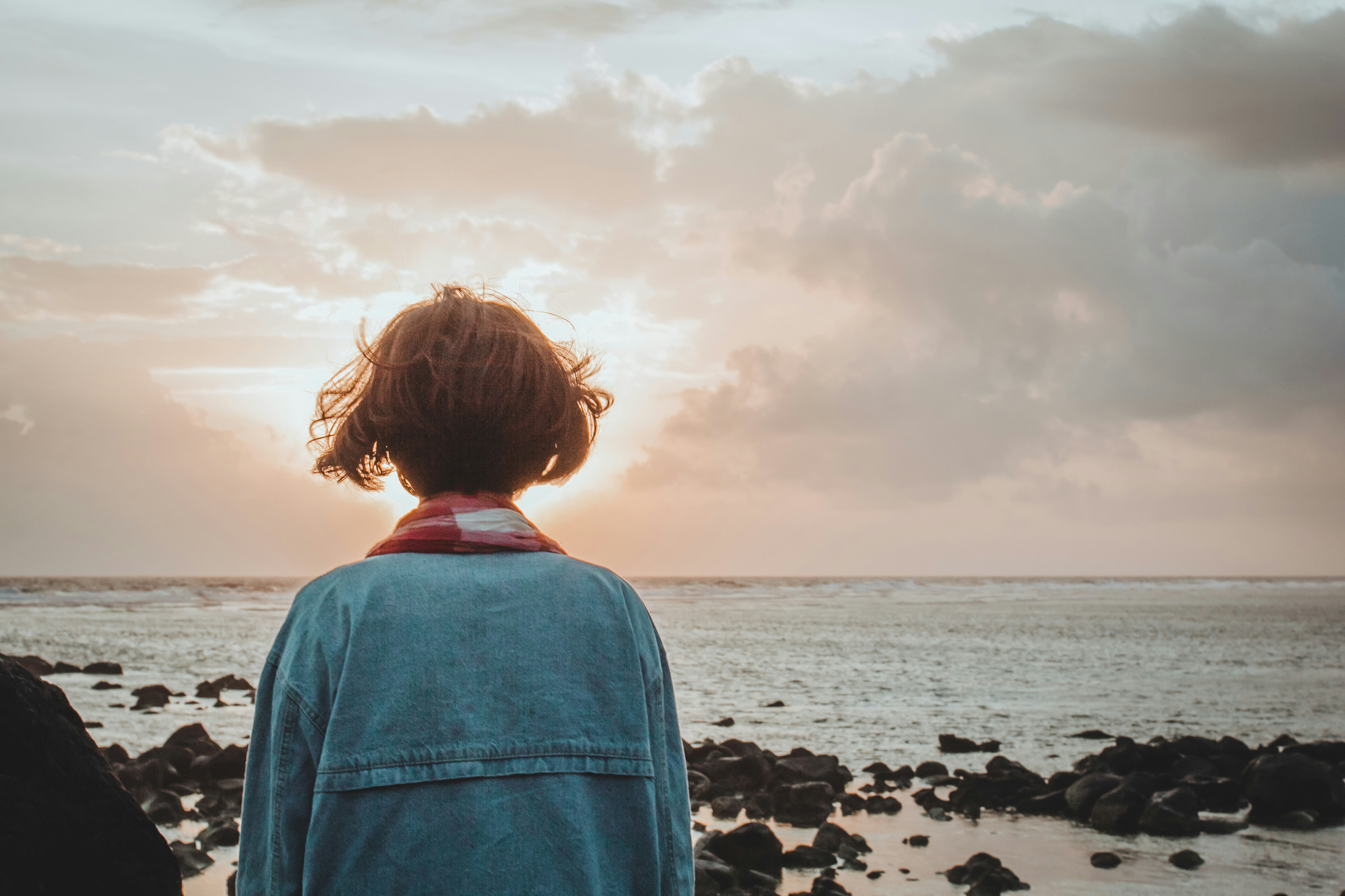 Una mujer mirando al mar y al horizonte en una puesta de sol