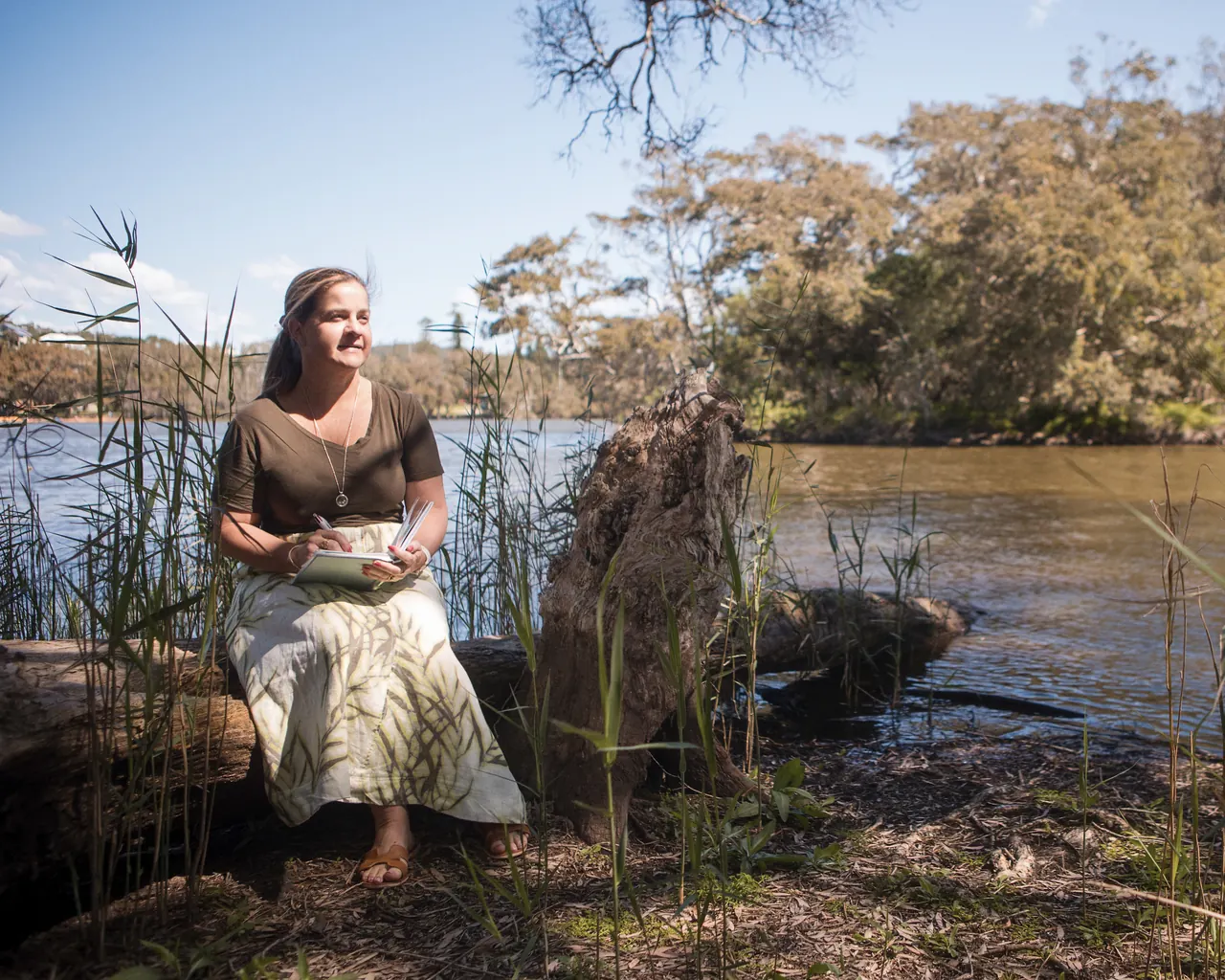 Tammy sitting by a Central Coast lagoon with a notebook, among the reeds
