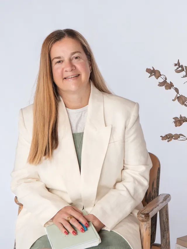 Tammy in a cream blazer beside a vase of dried eucalyptus