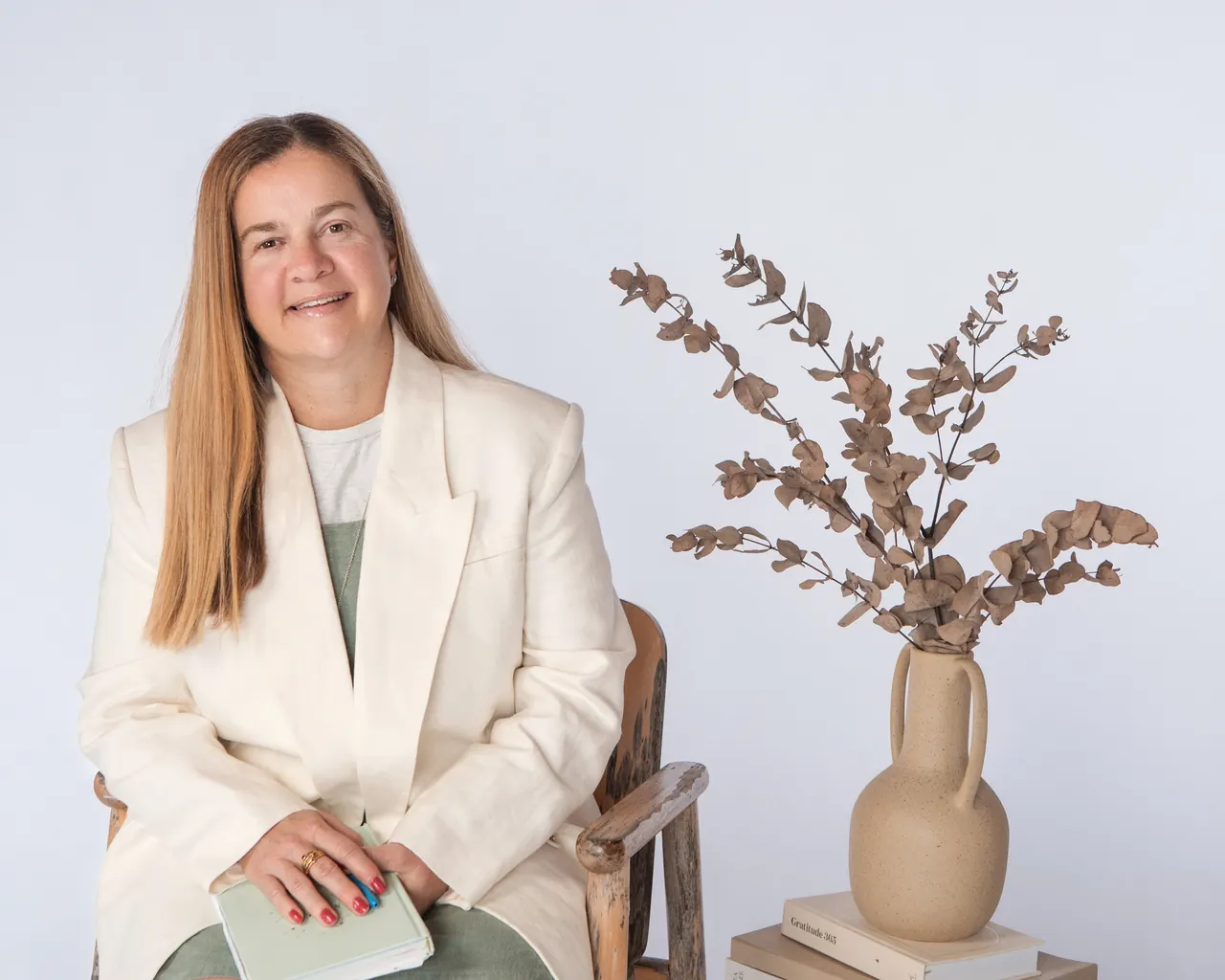 Tammy in a cream blazer, seated beside a vase of dried eucalyptus