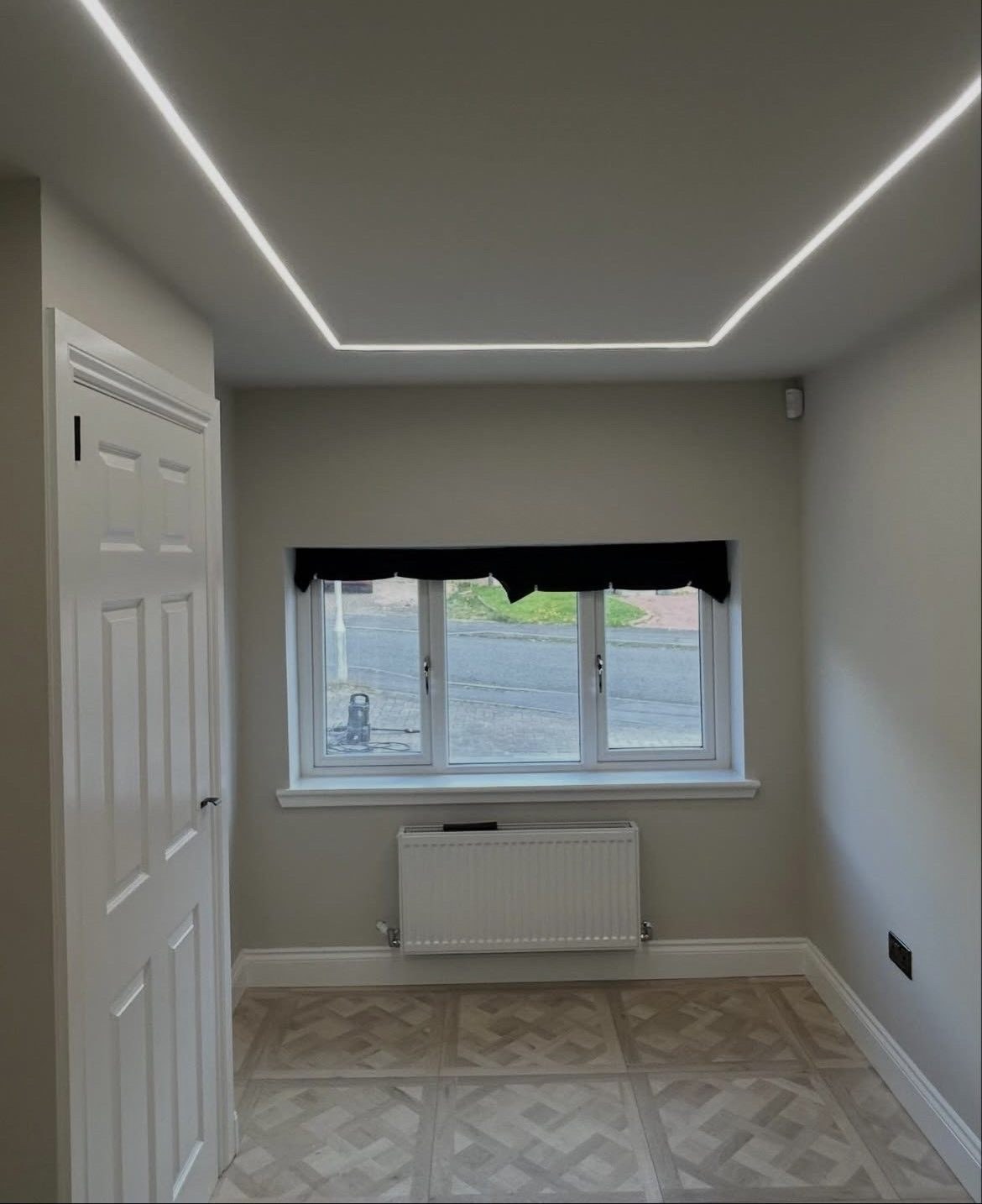Empty finished room with LED channel lighting around the ceiling and parquet-pattern floor