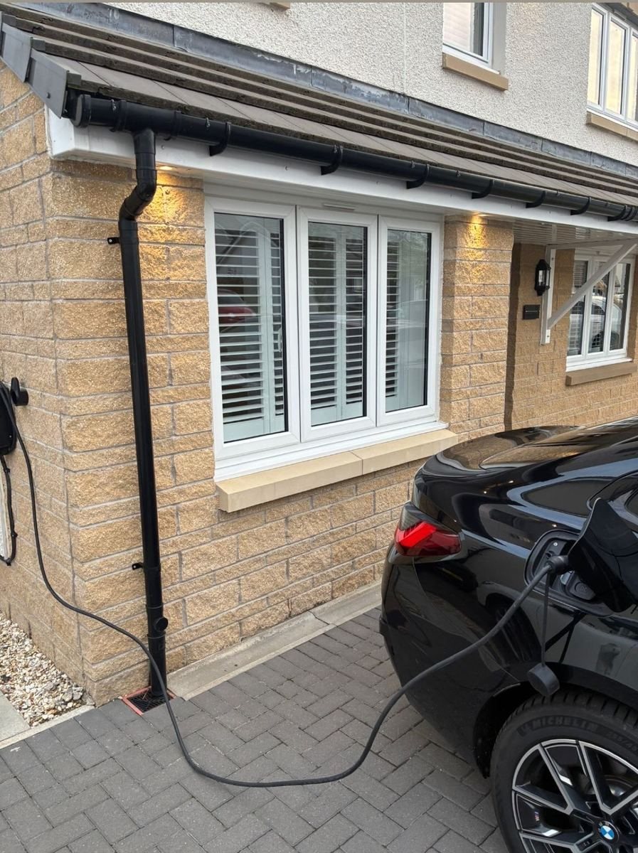 Wall-mounted EV charge point on a house wall with the cable run to a car on the driveway