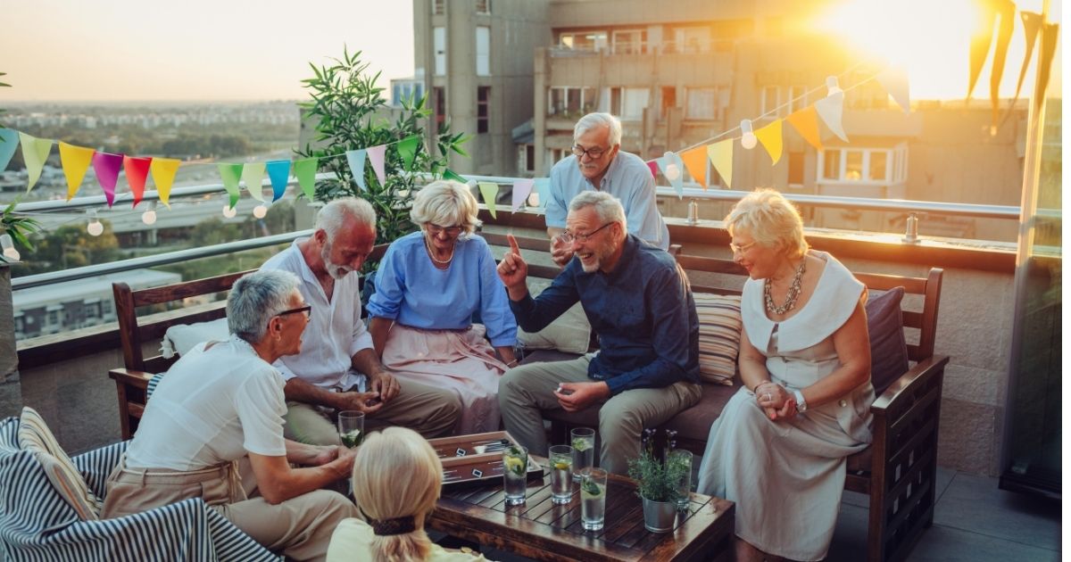 A group of adults in midlife gathered on an outdoor patio, laughing and talking together, representing friendship, connection, and community in midlife.