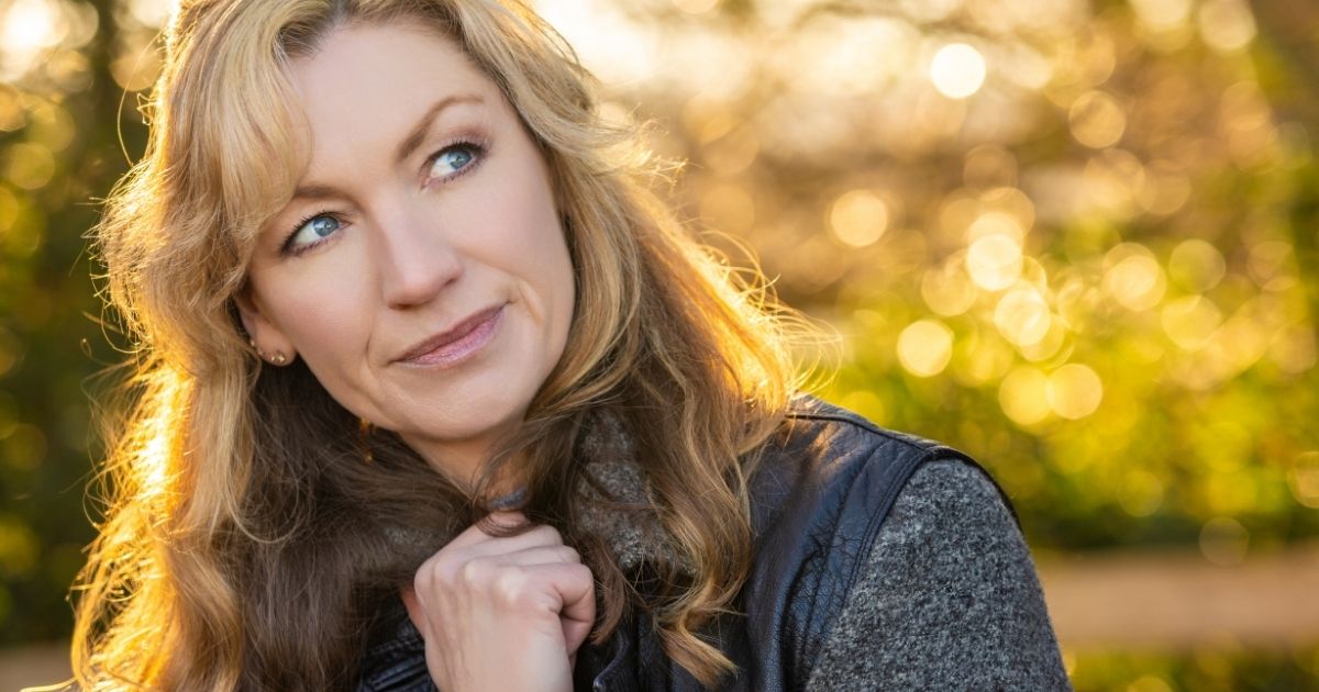 Midlife woman outdoors in soft sunlight, looking thoughtful and reflective as she considers her next chapter and what she wants in life