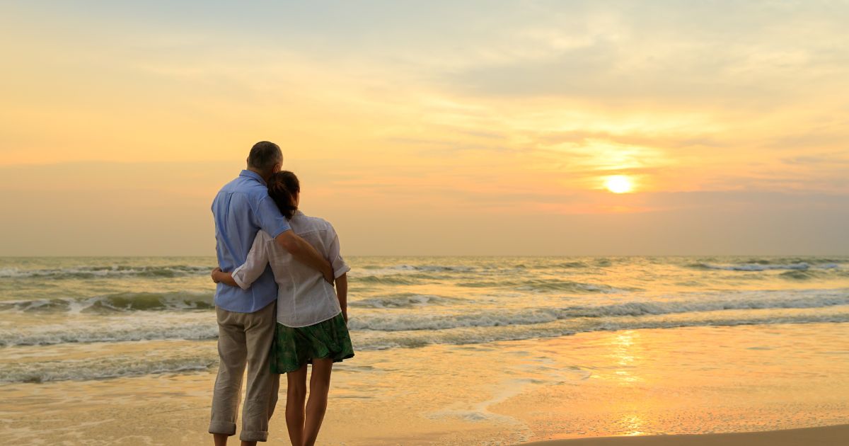 Midlife couple walking together on the beach at sunset, reflecting connection, healing, and healthy relationships in midlife