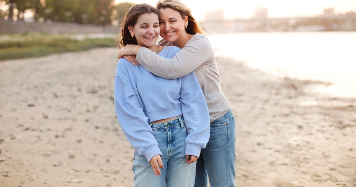 Midlife mother hugging her teenage or young adult daughter on the beach, representing communication and connection with adult children