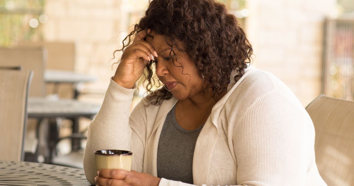 Midlife woman sitting alone with a worried expression, holding a coffee cup while experiencing anxiety and emotional overwhelm during perimenopause