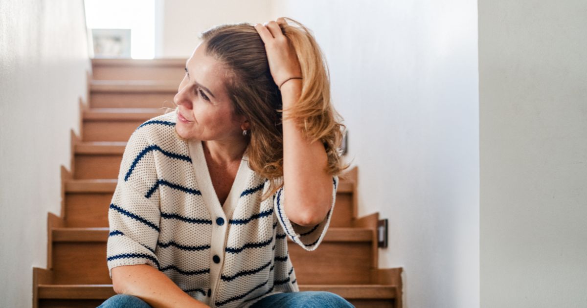 Midlife woman sitting on stairs looking thoughtful while reflecting on life changes and reconnecting with herself in midlife
