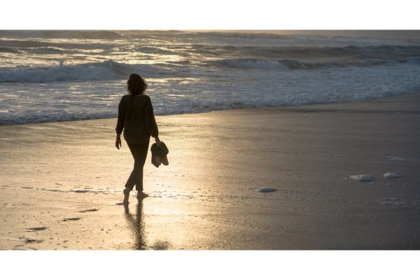 Woman walking alone along the beach at sunset, reflecting on personal growth, change, and shifting friendships.