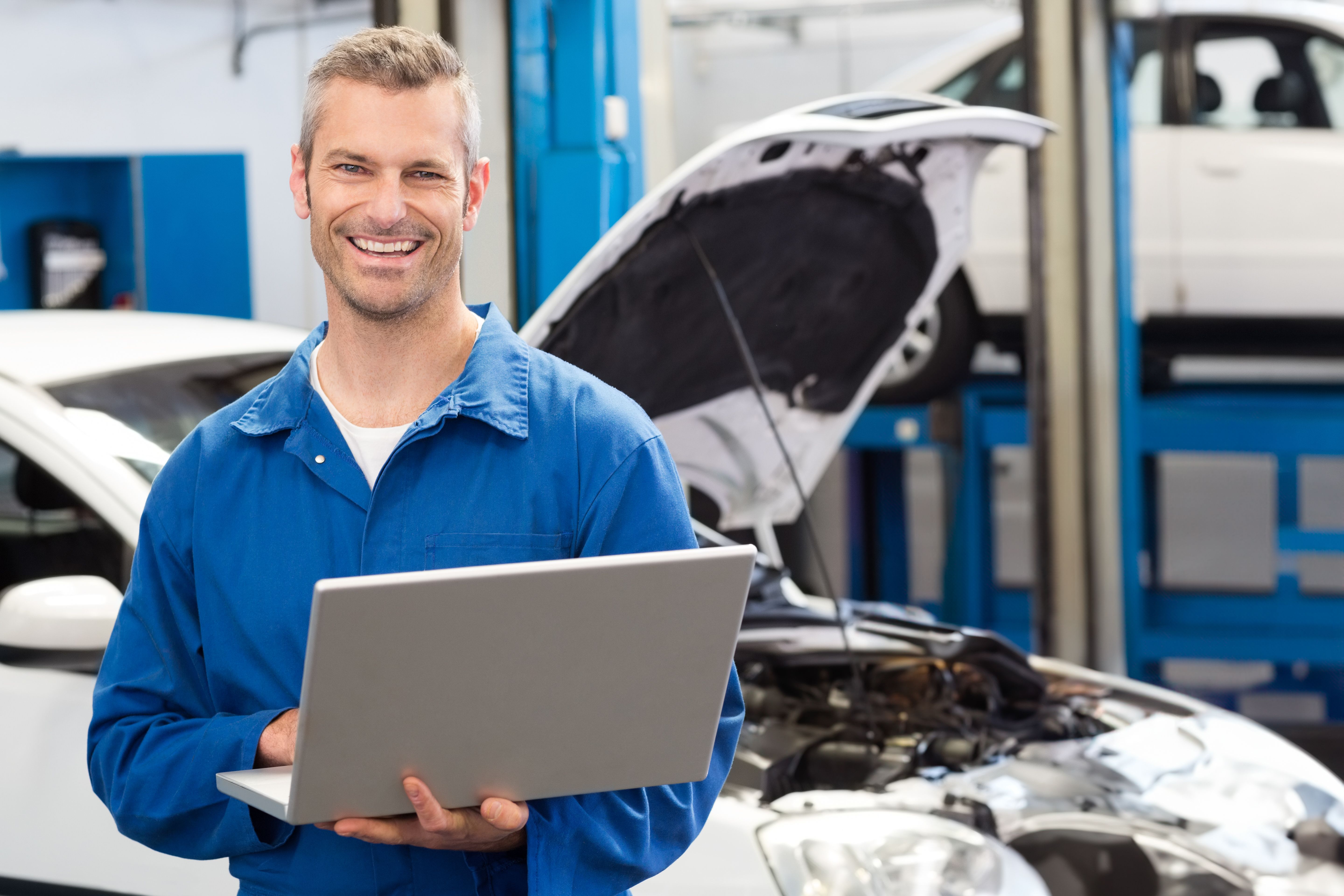 A mechanic kneeling beside a car in an Australian workshop, phone ringing on bench