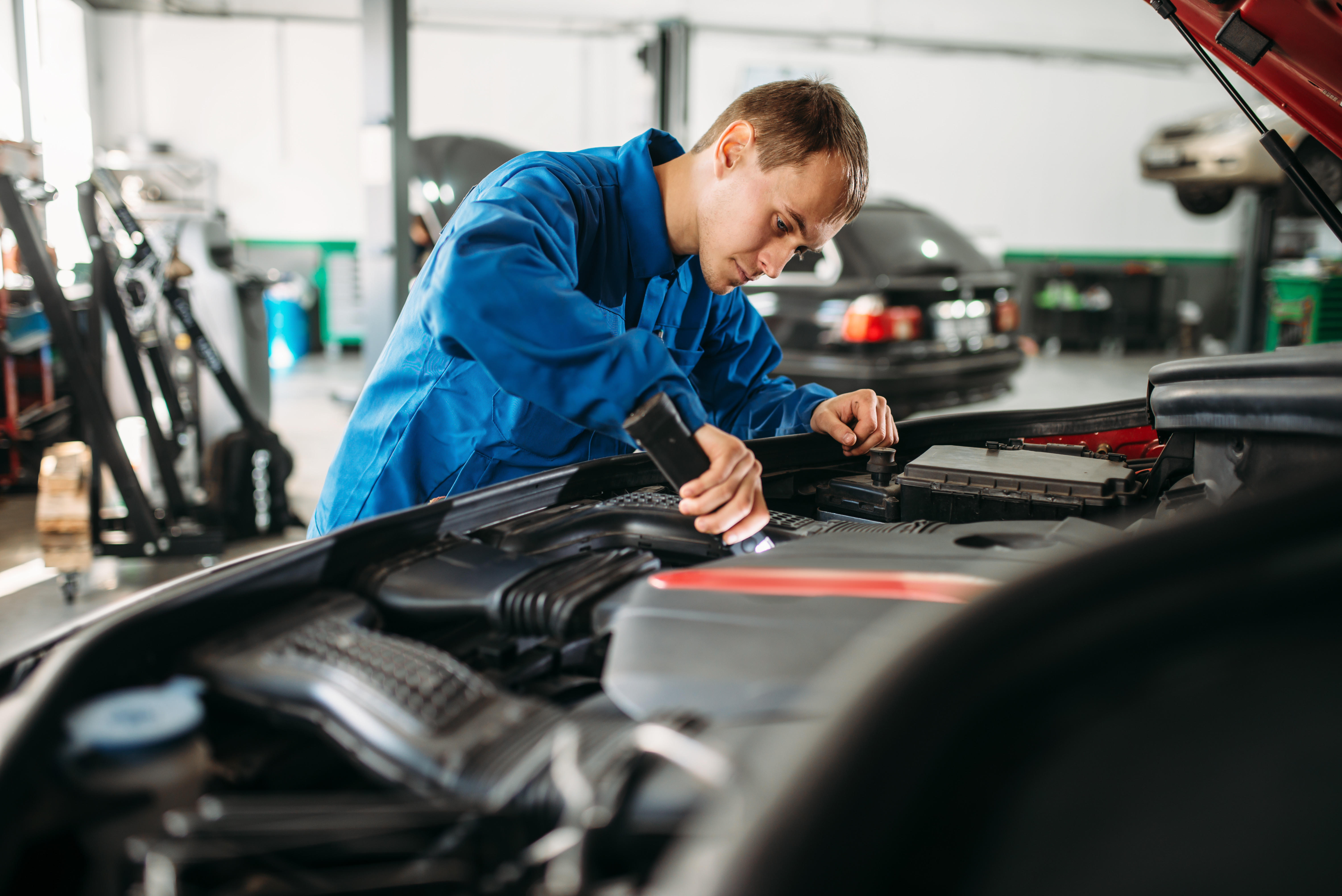 A mechanic kneeling beside a car in an Australian workshop, phone ringing on bench