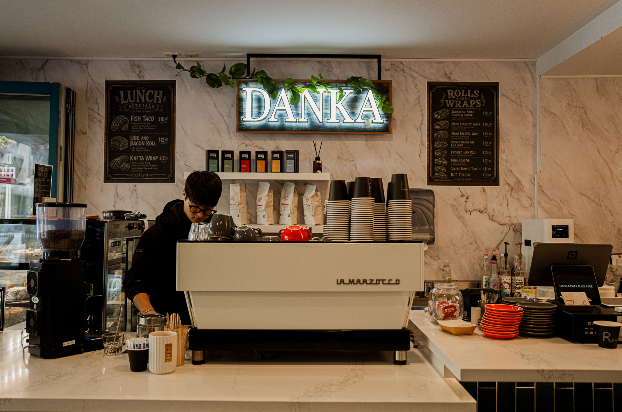 A Danka barista at the La Marzocco espresso machine beneath the glowing DANKA neon sign