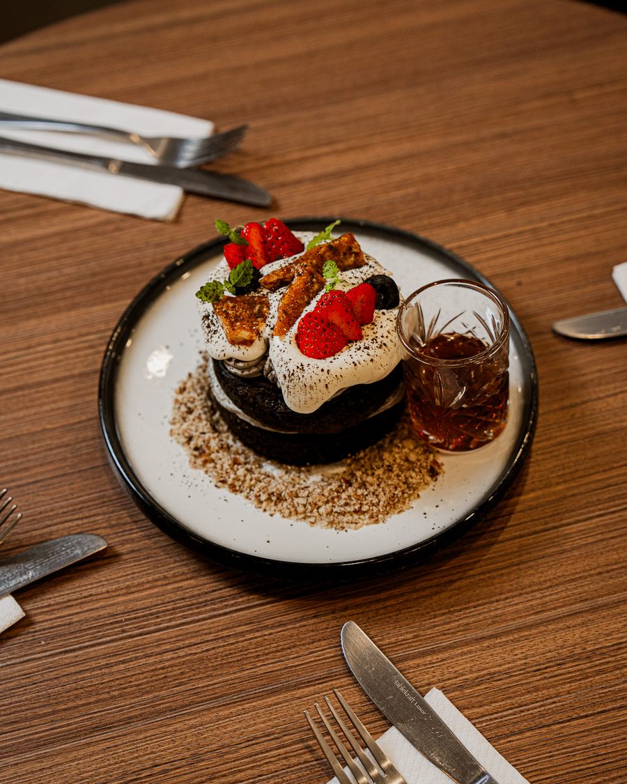 Stack of Hojicha Hotcakes topped with black sesame cream, strawberries and hazelnut brittle