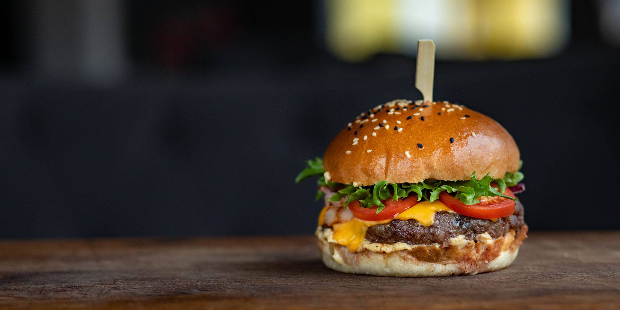 A cheeseburger with lettuce, tomato and melted cheddar on a wooden board