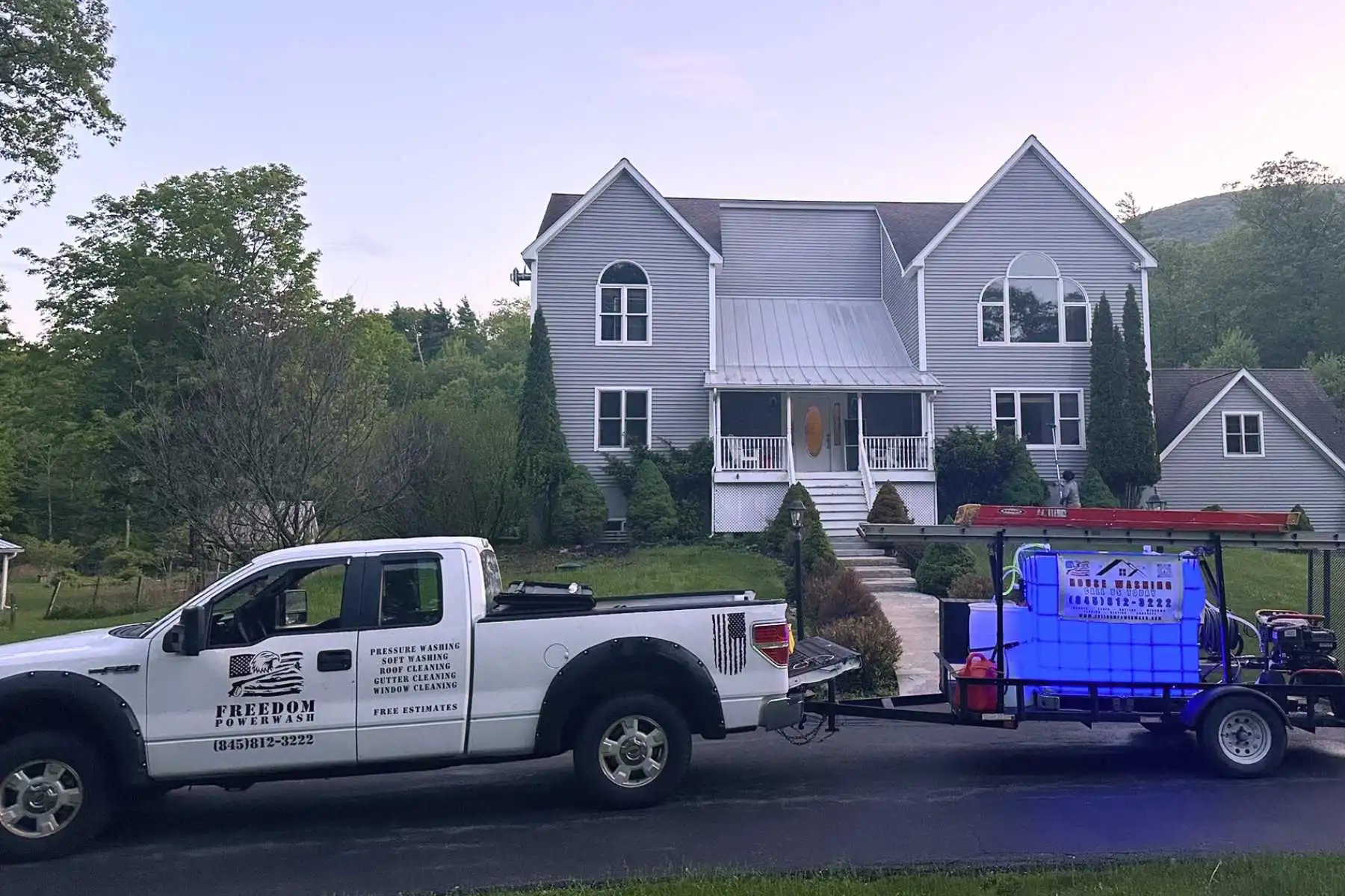 Freedom Powerwash truck and soft wash trailer parked in front of a large residential Hudson Valley home at dusk.