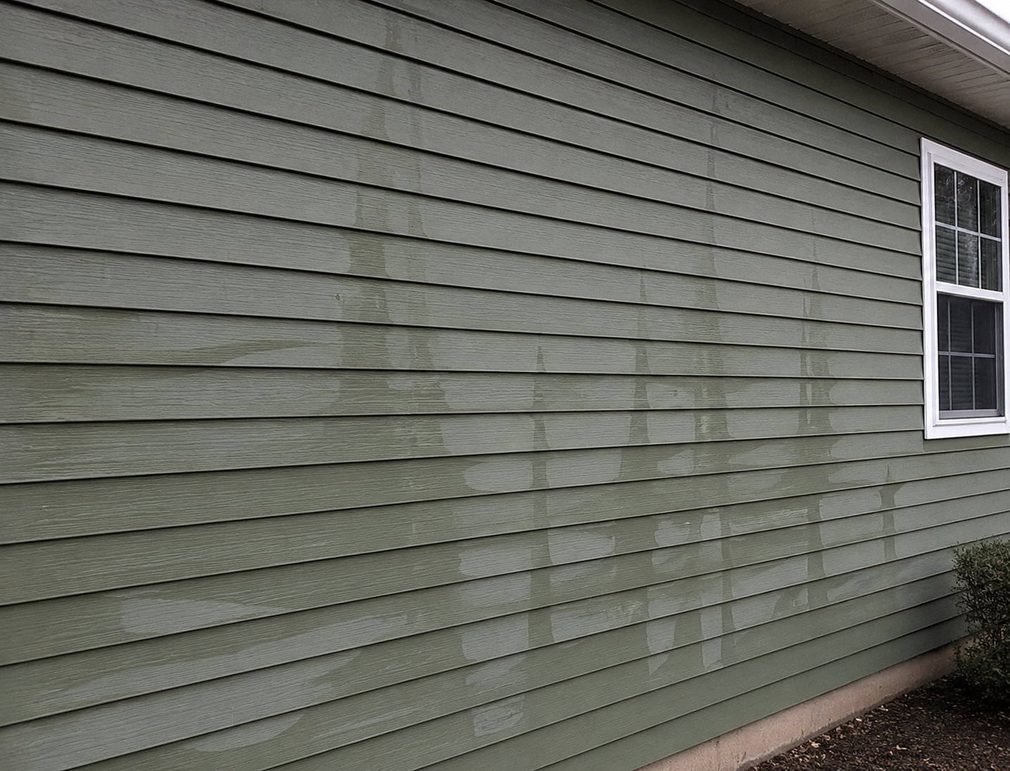 Vinyl siding damaged by improper pressure washing showing visible wand marks, oxidation streaks, and uneven cleaning lines on a residential home exterior.