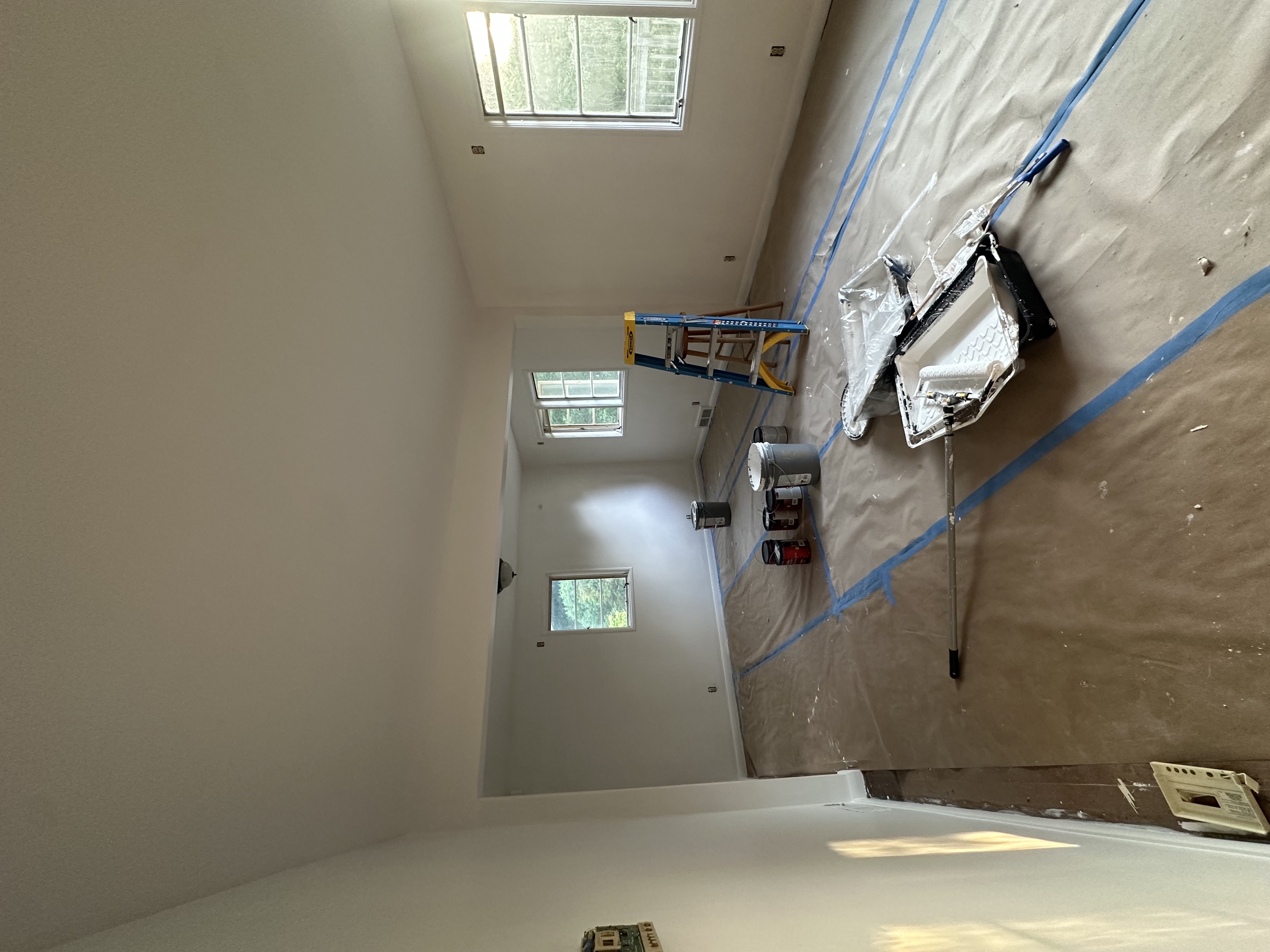 Empty room with floors fully covered in drop paper and painting supplies set up