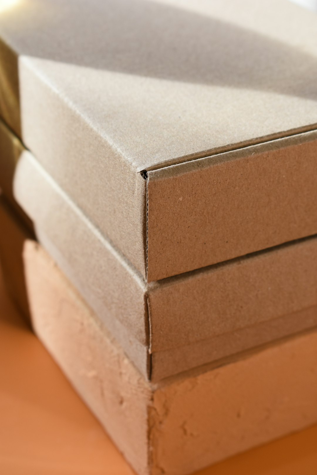 Close-up of three flat brown cardboard mailer boxes stacked on a warm-toned surface in soft light.