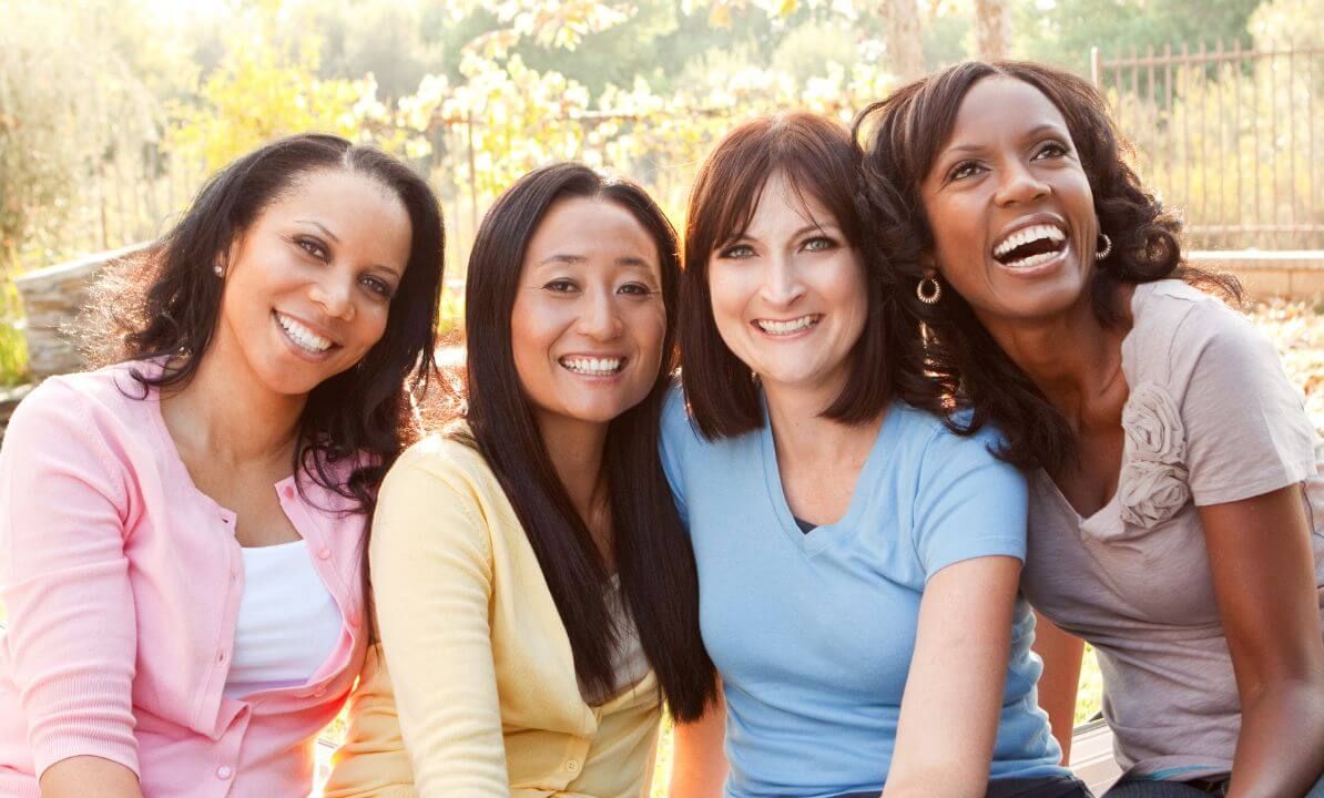 Four multi-cultural midlife women grouped together, smiling