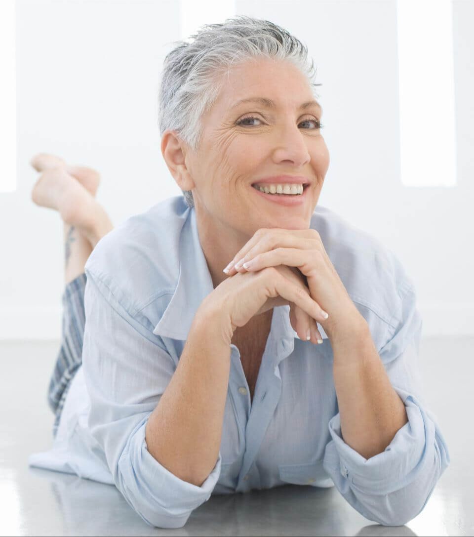 Middle aged woman reclining on her stomach, chin on hands, smiling at the camera