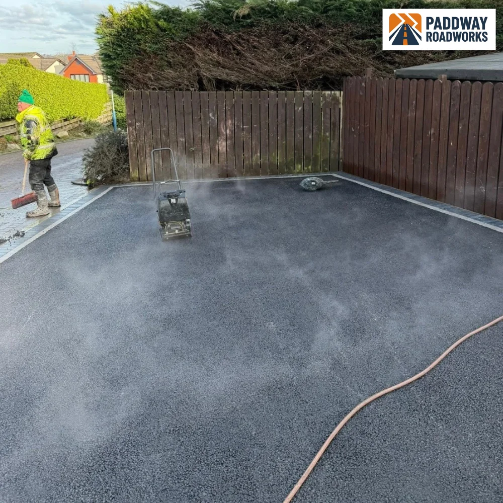 Tarmac driveway being rolled mid-install (worker visible from behind, no face).