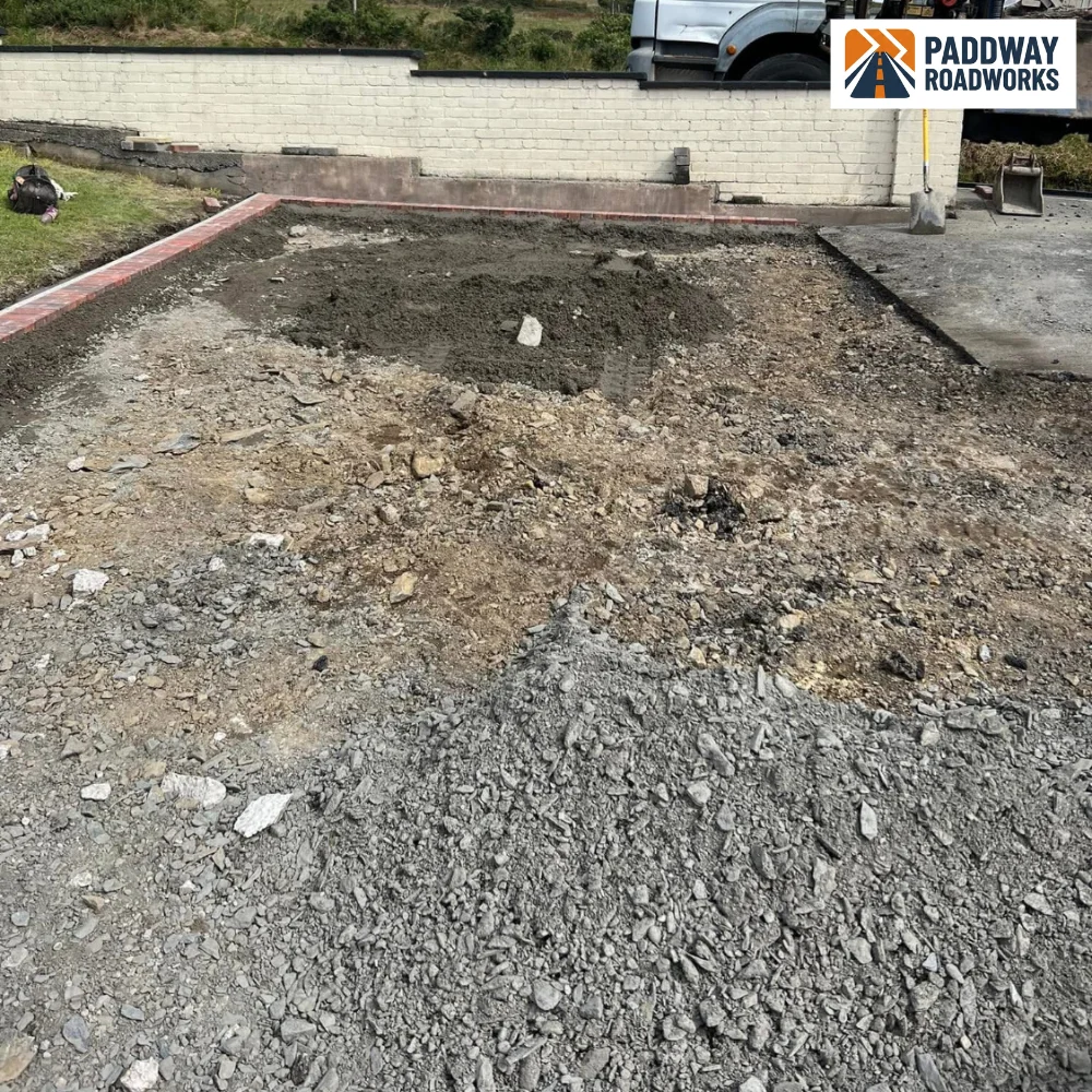 BEFORE — excavation: dirt, rubble and stone aggregate piled, white site van visible.