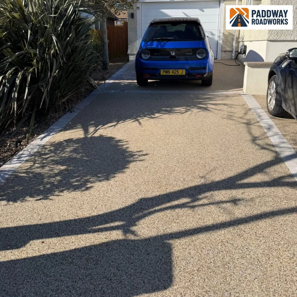 Honey-tone resin-bound driveway with blue car parked, granite border edging.