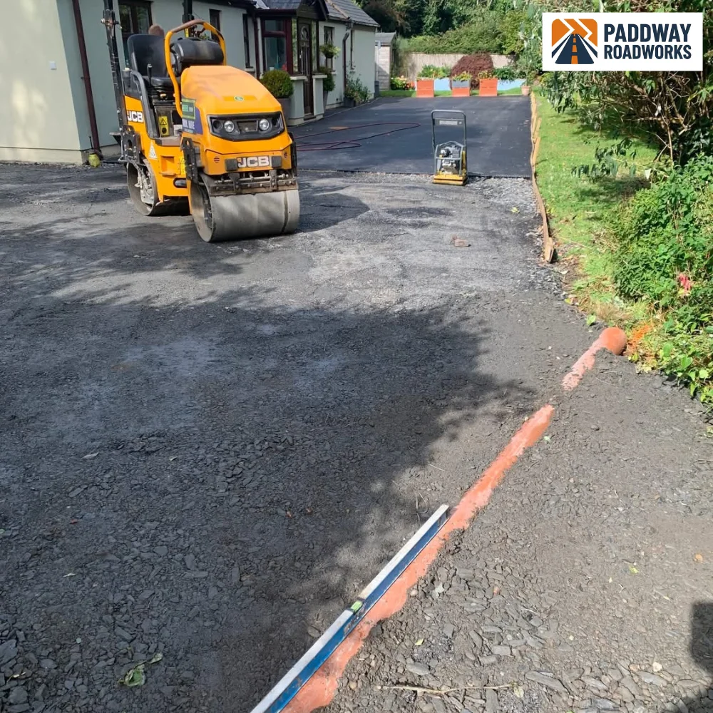 Yellow JCB tandem road roller compacting freshly laid tarmac.