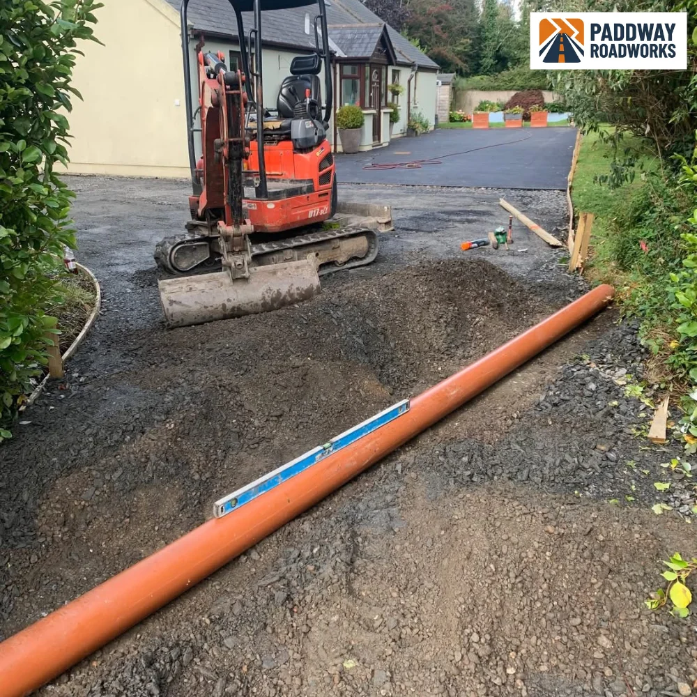 Drainage trench with orange uPVC pipe being installed, red Kubota mini-excavator beside.