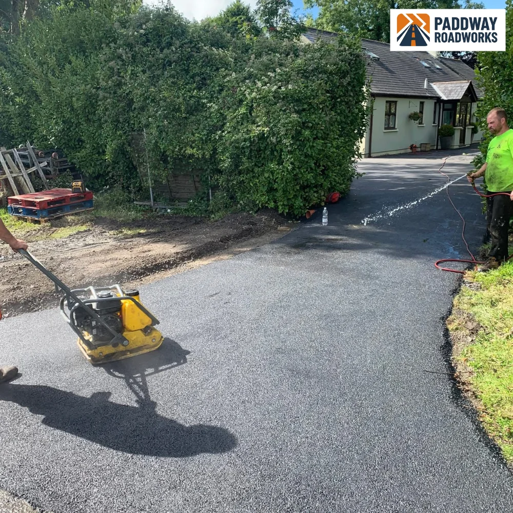 Worker compacting tarmac with petrol vibrating plate — captured from the side mid-work, no face.