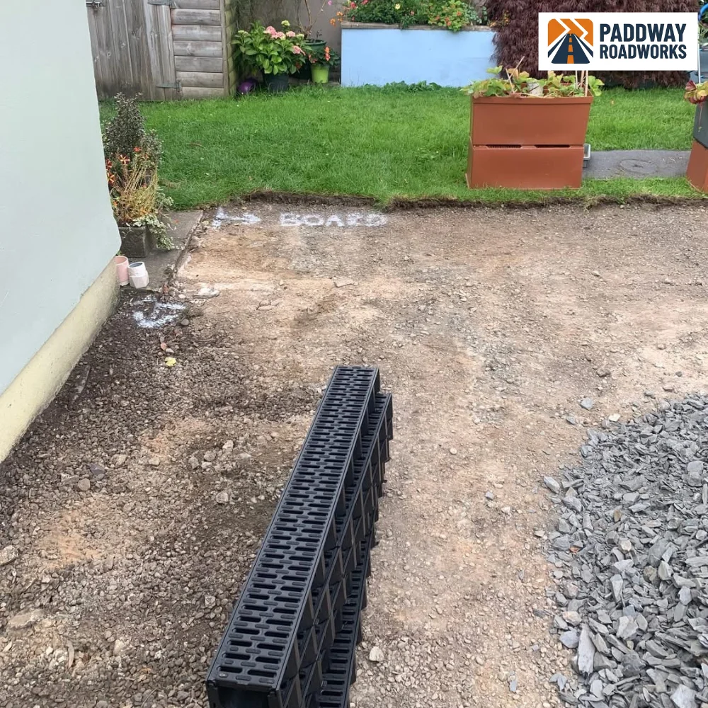 Black plastic linear drainage channel sections staged for install.