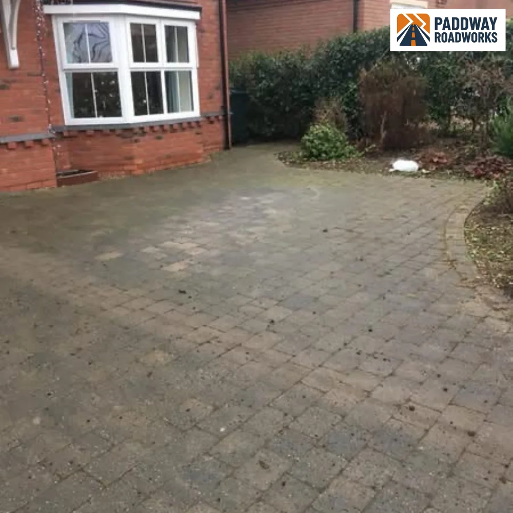 Block-paved driveway in front of red brick bay-window house.