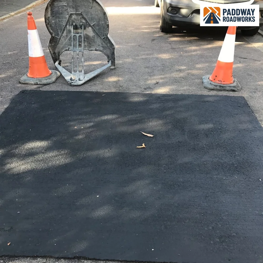 Pothole repair complete — small black tarmac patch with traffic cones.