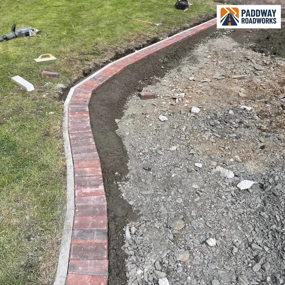 Red brick kerb laid in a sweeping curve, ground prep mid-install.
