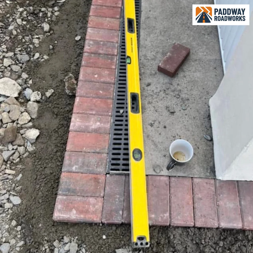 Block paving install detail — kerb laid alongside spirit-level showing precision.