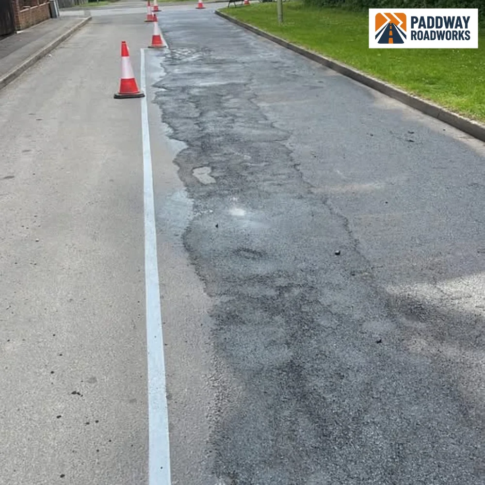 Slurry-sealed road with painted line markings and traffic cones.