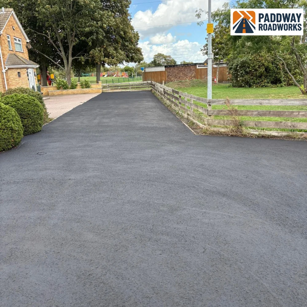 Tarmac driveway finished in front of country house with mature garden.